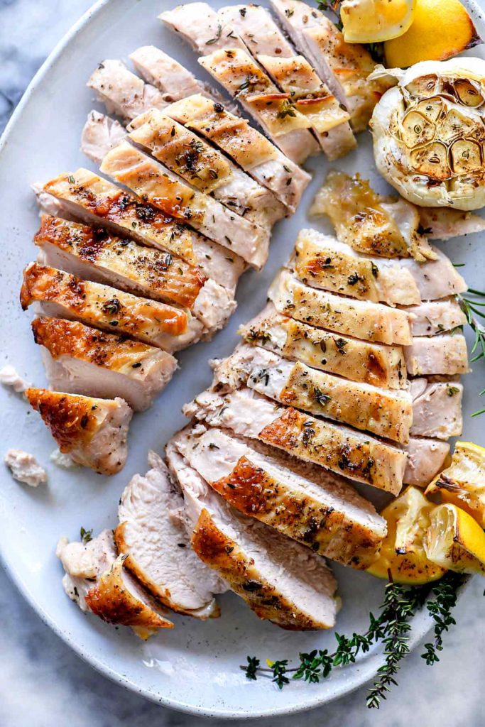 sliced roast turkey breast on white platter with roasted clove of garlic and fresh herbs
